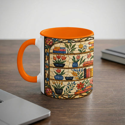 White mug with orange handle featuring a stained-glass design of bookshelves and flowers.