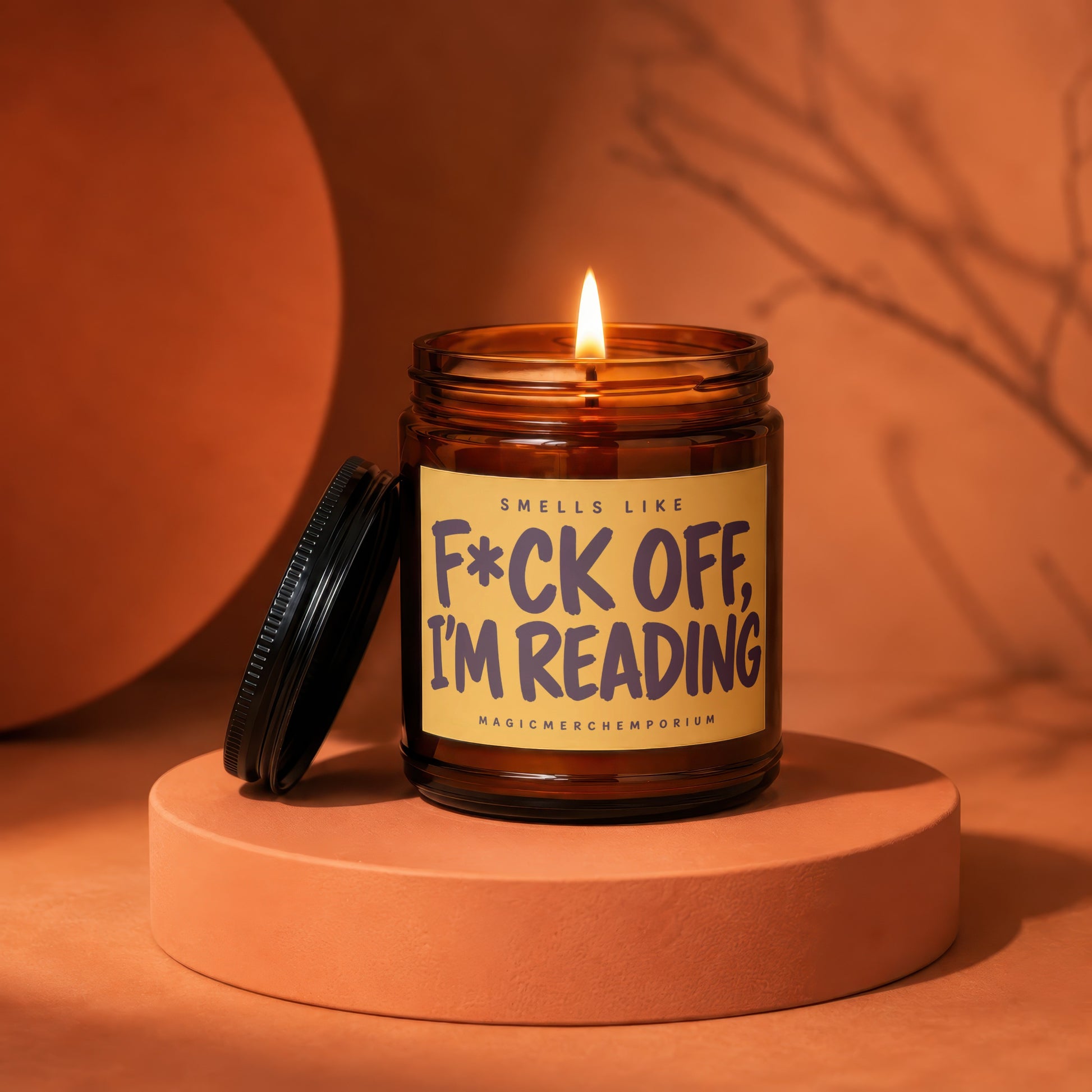 Amber jar candle with lit wick and "F\*ck off, I'm reading" label.