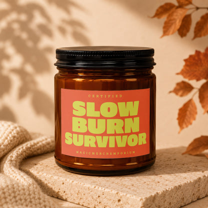 Amber candle with black lid, orange label reading "Slow Burn Survivor."