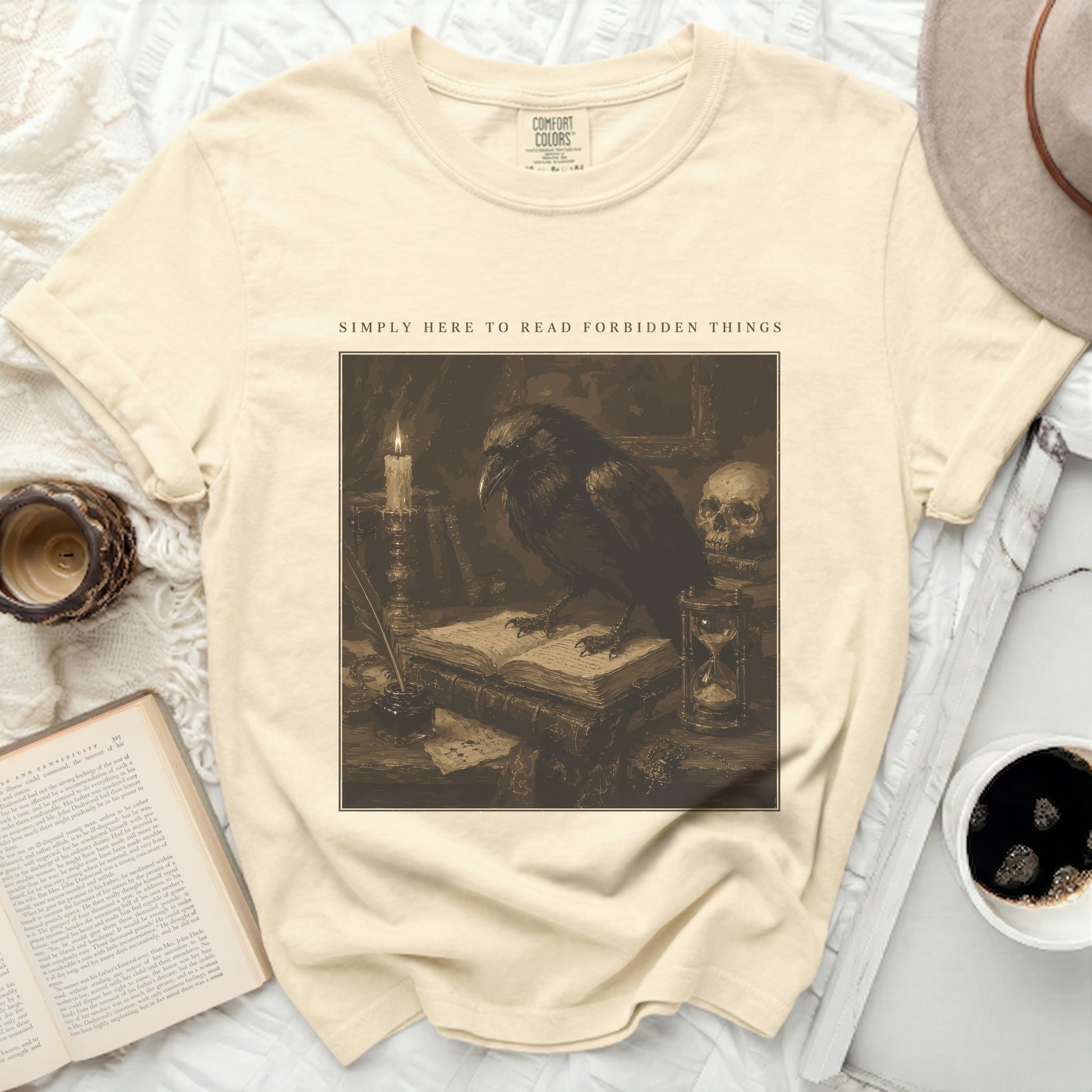 Cream shirt with a raven reading on books and text "SIMPLY HERE TO READ FORBIDDEN THINGS".