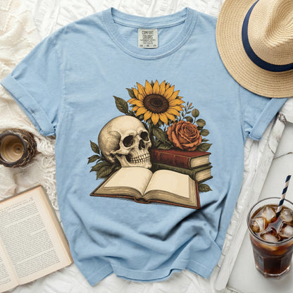 Light blue t-shirt with skull, sunflower, rose, and open books graphic.