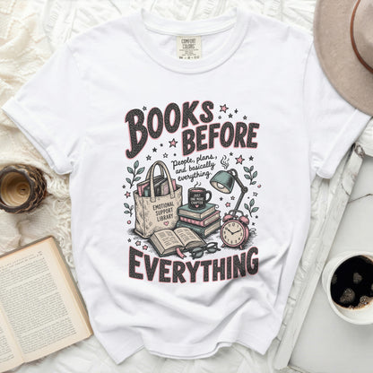 White t-shirt graphic with "Books Before Everything" text and book-themed illustrations.