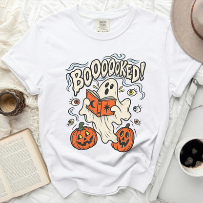 White t-shirt with "BOOOOKED!" text, ghost, pumpkins, and eyes graphic.