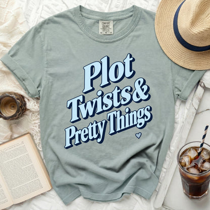 Light blue t-shirt with "Plot Twists & Pretty Things" text and a small heart.