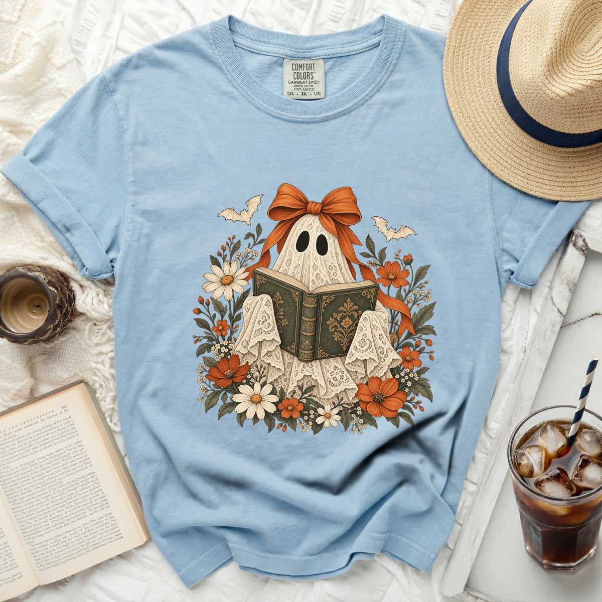 Light blue t-shirt with a ghost reading a book, surrounded by flowers and bats.