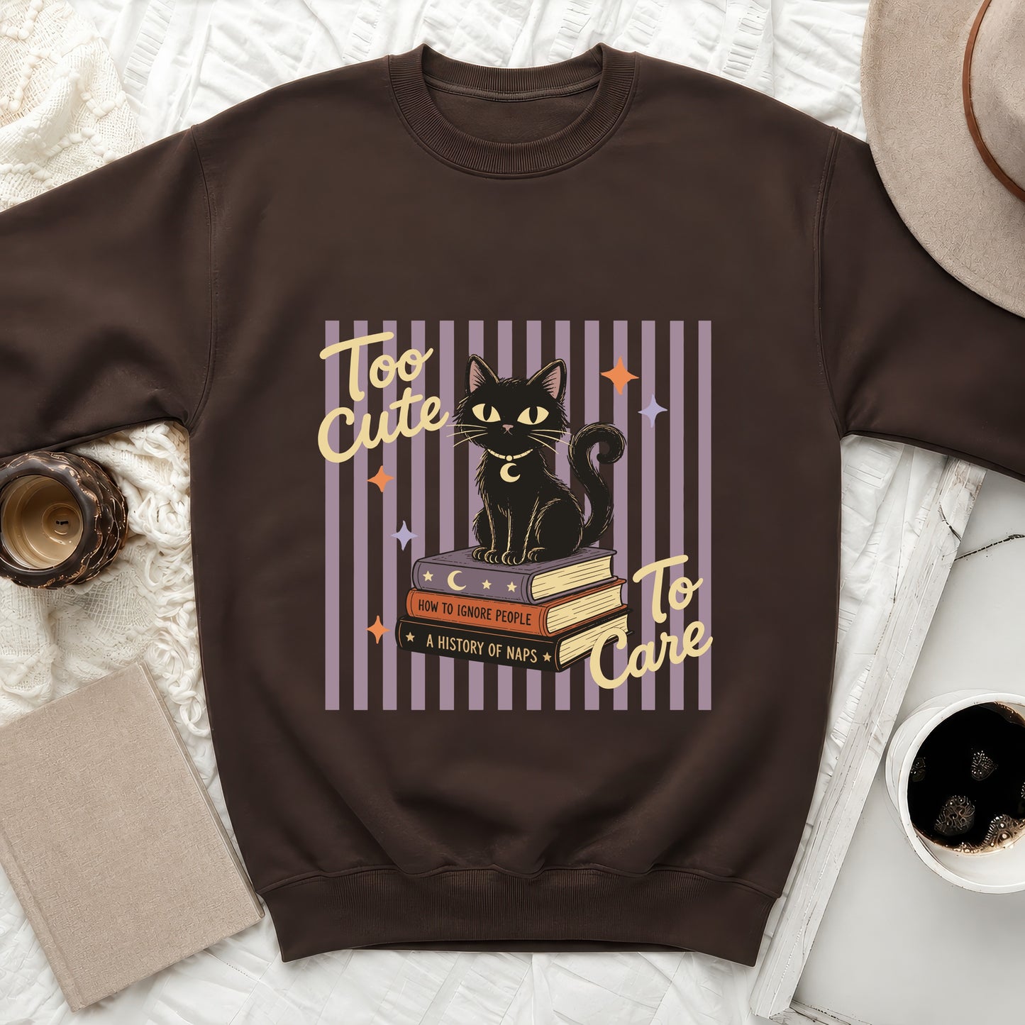 Brown sweatshirt with a graphic of a black cat on books reading "Too Cute To Care".