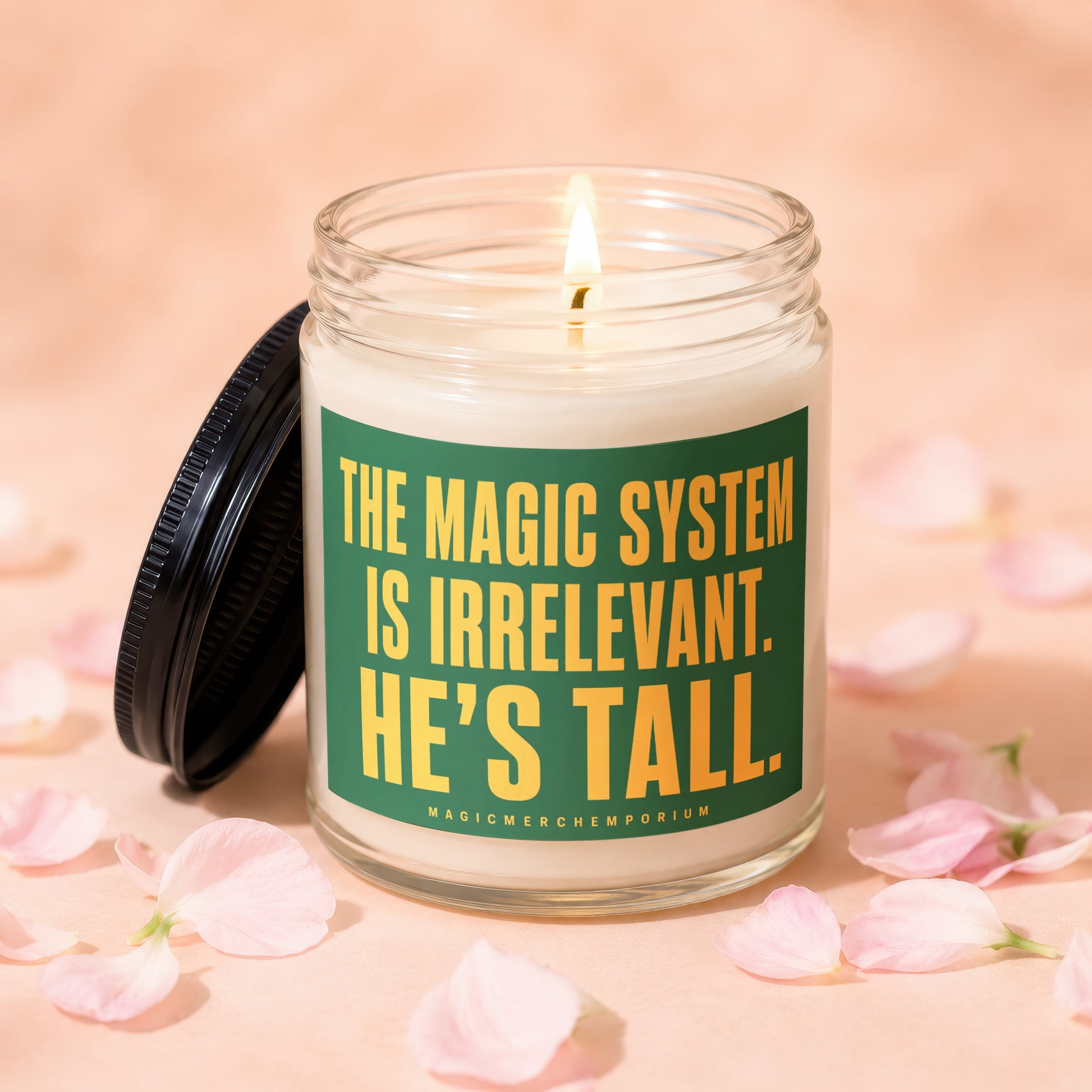 Glass candle with lit wick and green label reading "The magic system is irrelevant. He's tall."
