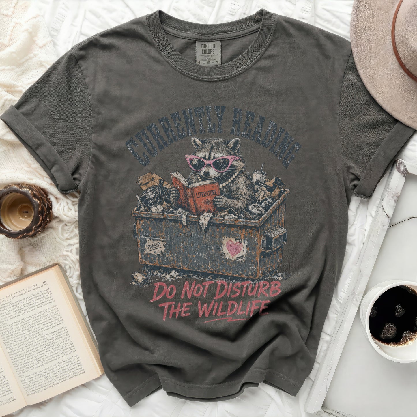 Graphic t-shirt with raccoon reading in trash can, "Do Not Disturb The Wildlife".