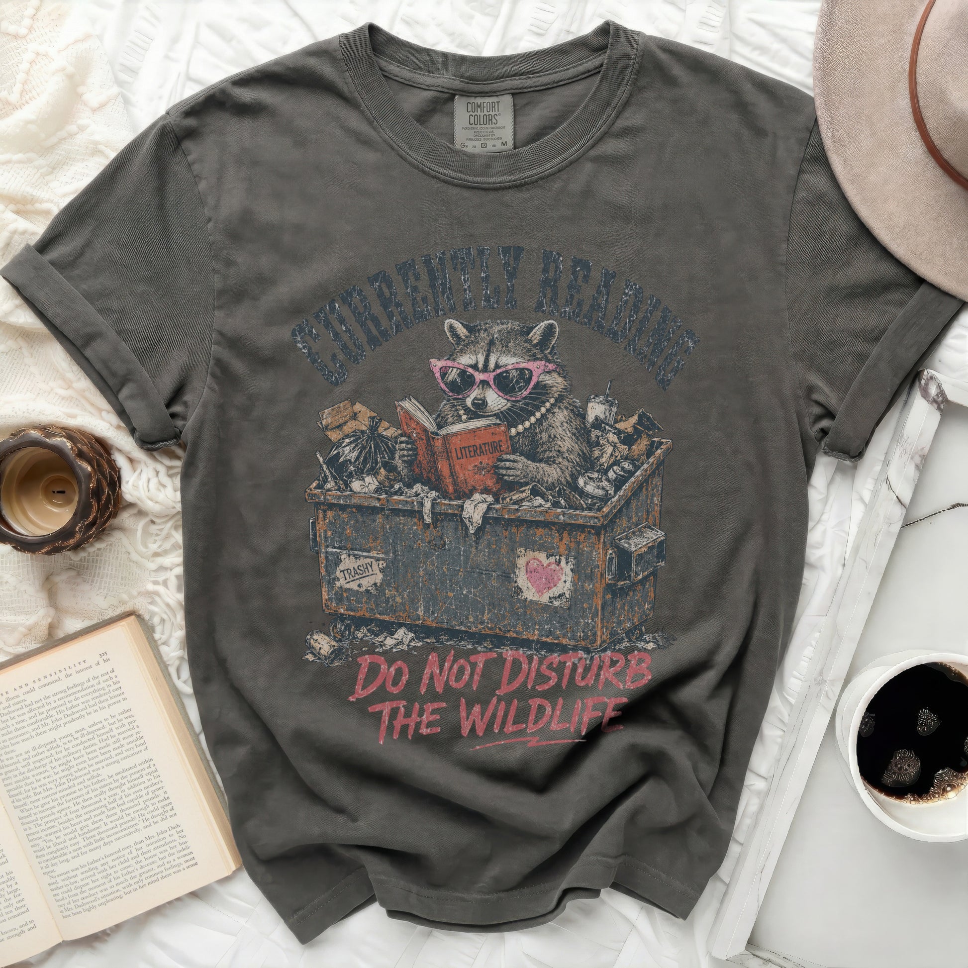 Graphic t-shirt with raccoon reading in trash can, "Do Not Disturb The Wildlife".