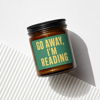 Brown glass candle with green label reading "Go Away, I'm Reading".