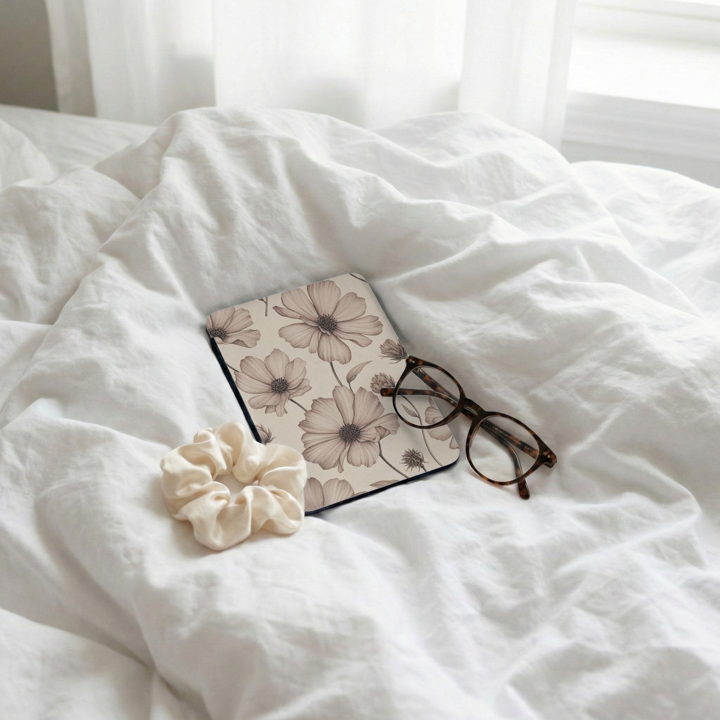 Floral patterned notebook, scrunchie, and glasses on white wrinkled sheets.