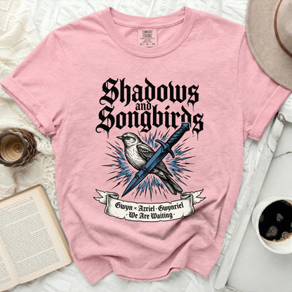 Pink t-shirt with "Shadows and Songbirds" text and a bird with a sword.