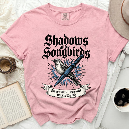 Pink t-shirt with "Shadows and Songbirds" text and a bird with a sword.