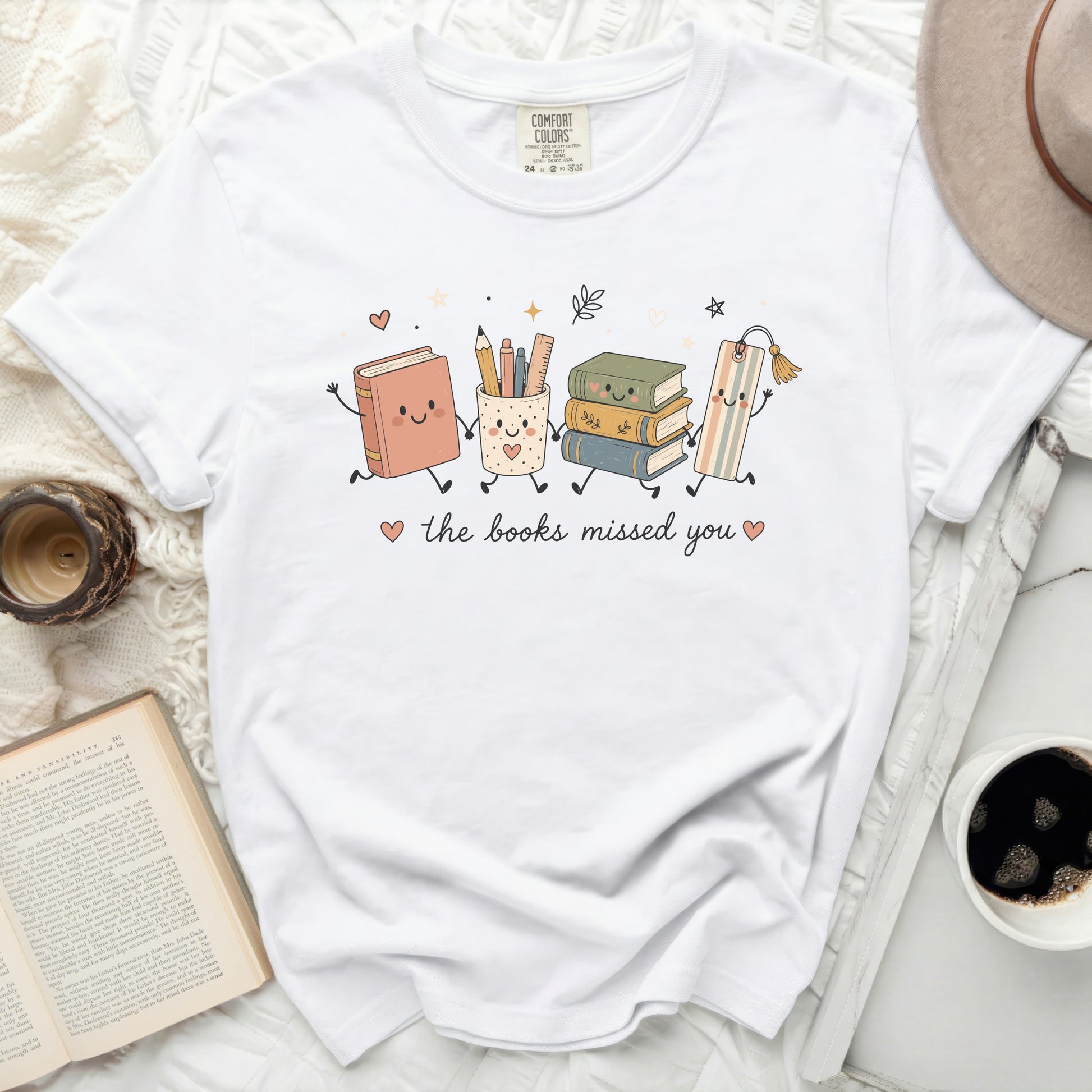 White t-shirt with graphic of happy books and school supplies characters saying "the books missed you".