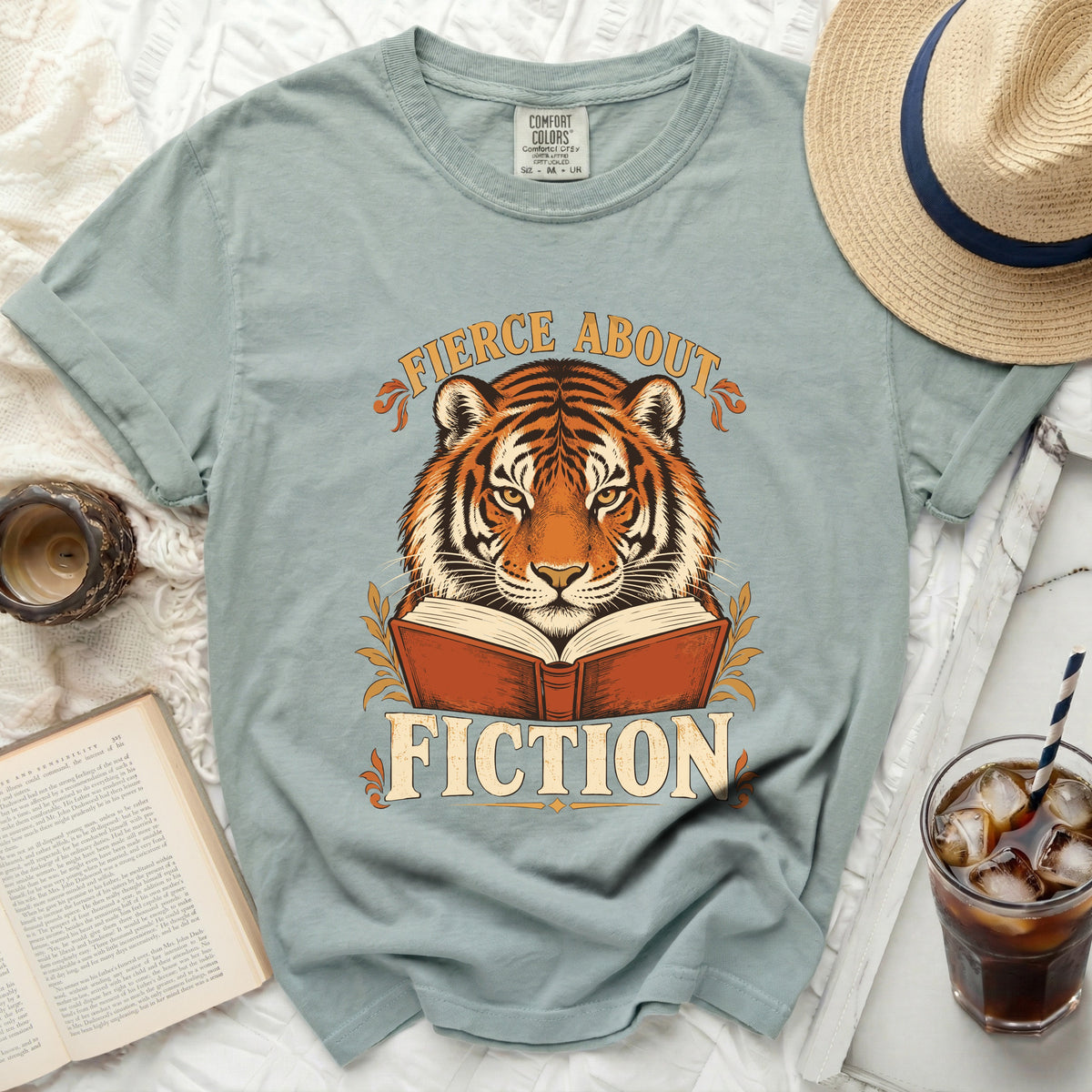 Tiger reading a book with text "Fierce About Fiction" on a t-shirt.
