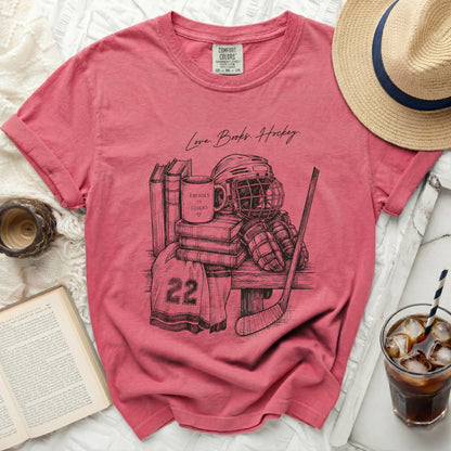 T-shirt with sketch of hockey gear, books, and mug reading "Enemies to Lovers."
