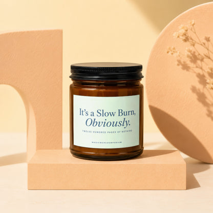 Amber candle in a jar with a black lid, labeled "It's a Slow Burn, Obviously."