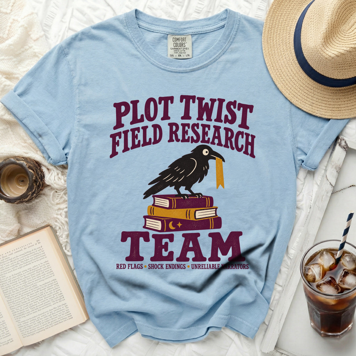 Light blue t-shirt with crow on books and text "Plot Twist Field Research Team".