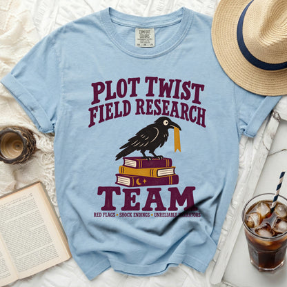 Light blue t-shirt with crow on books and text "Plot Twist Field Research Team".