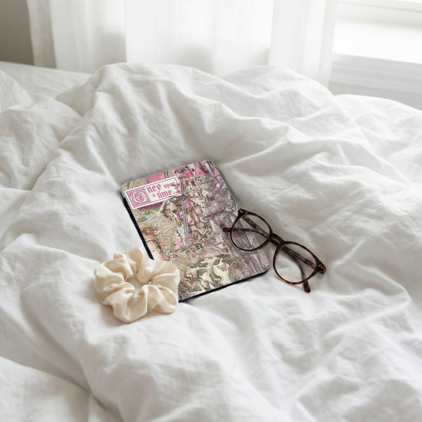 Journal with "Once upon a time" text, glasses, and scrunchie on rumpled white sheets.