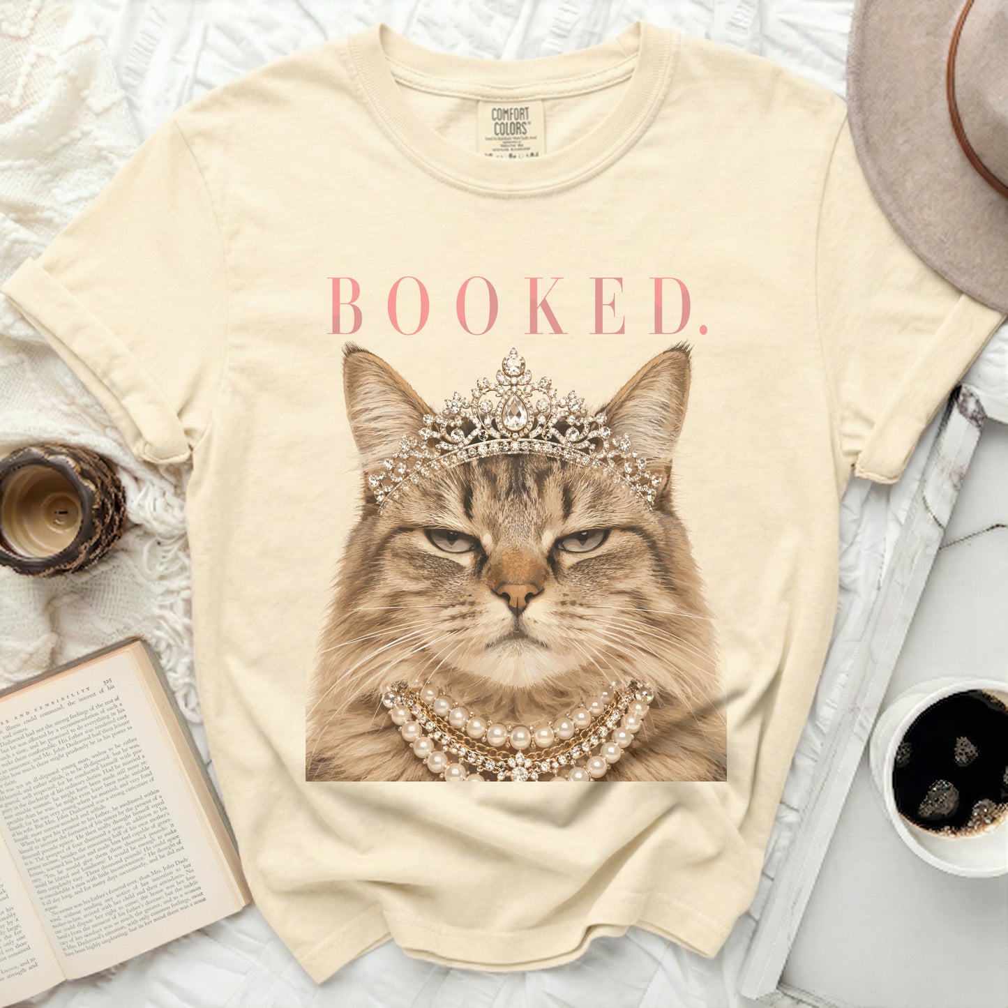 Cream t-shirt with regal cat wearing crown and pearls, text BOOKED.