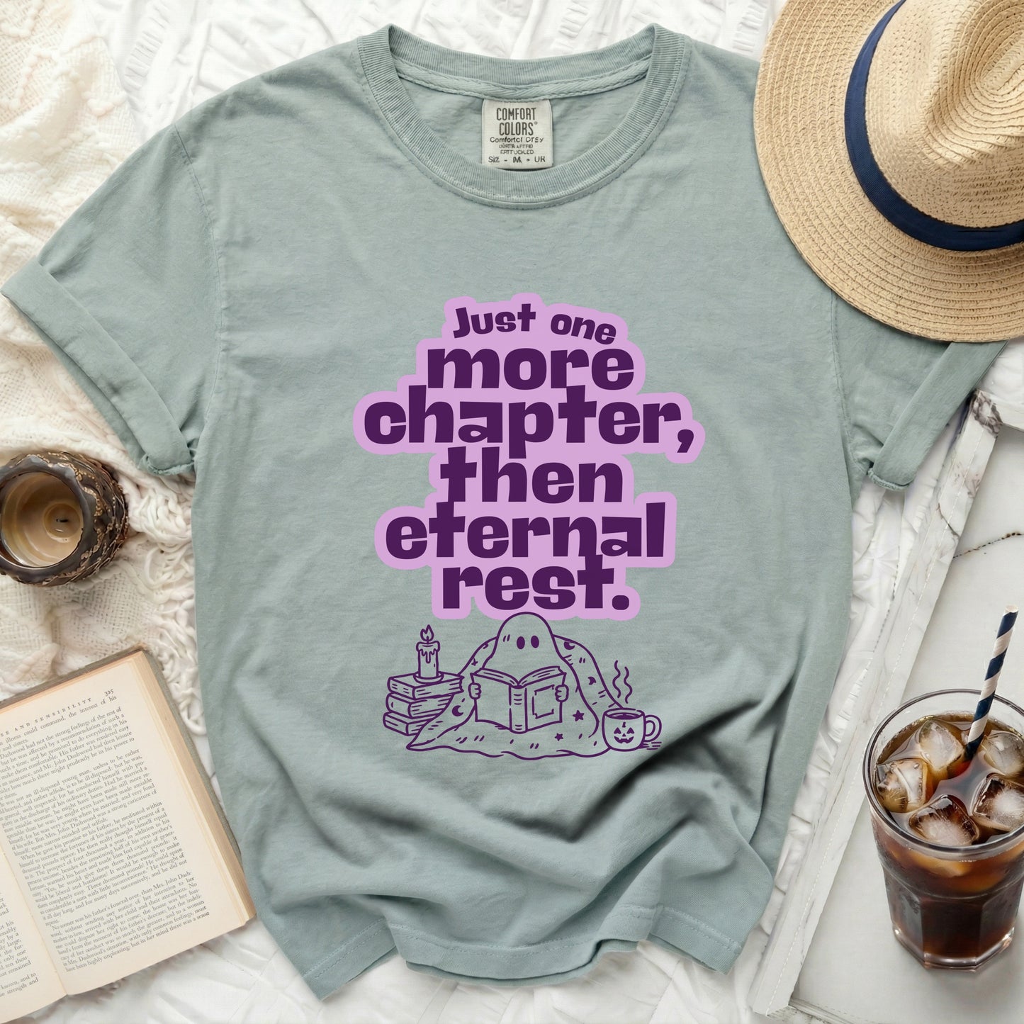 A sage green t-shirt with a ghost reading and the text "Just one more chapter, then eternal rest."