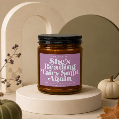 Candle with lavender label reading "She's Reading Fairy Smut Again".
