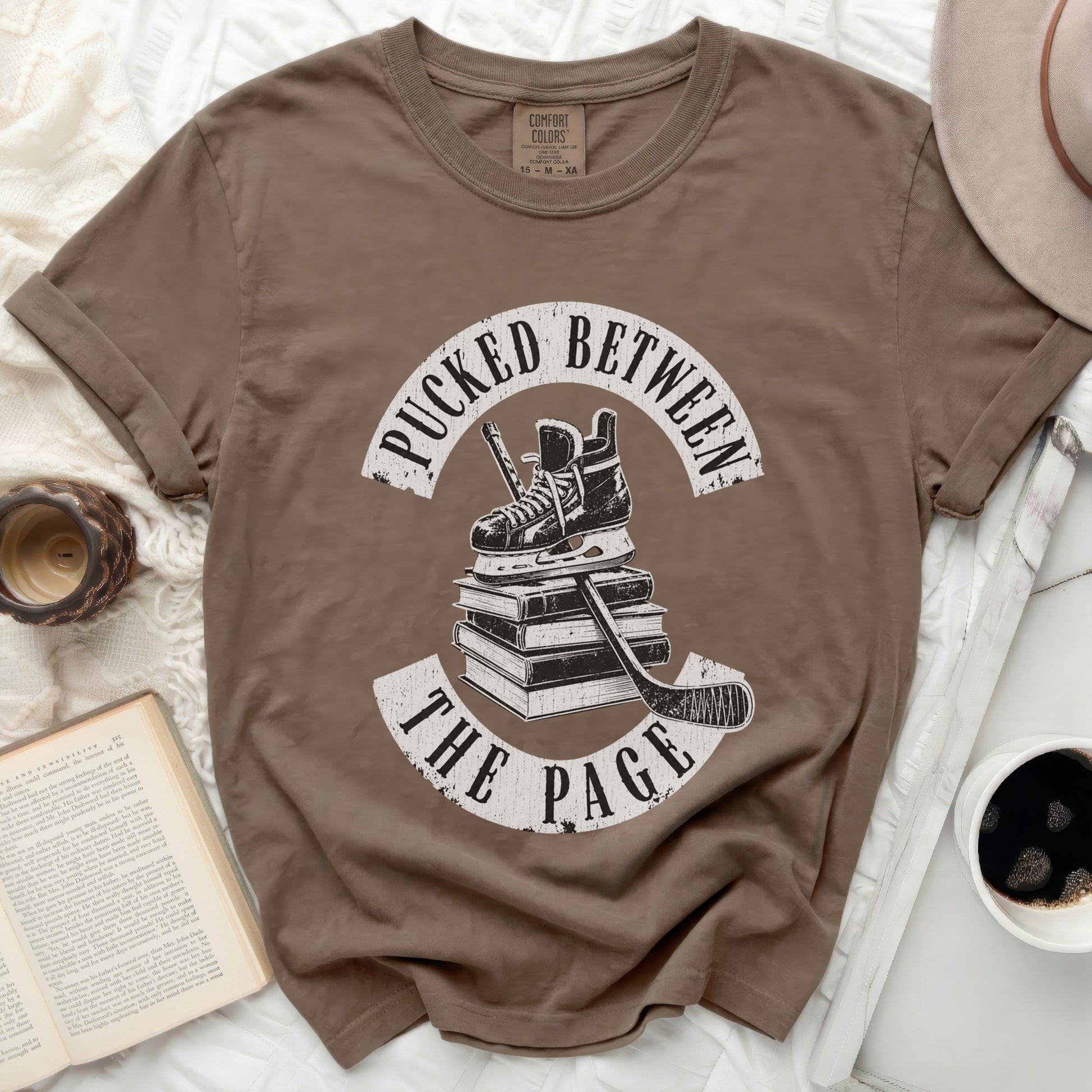 Brown t-shirt with "Pucked Between The Page" text and hockey gear graphic.