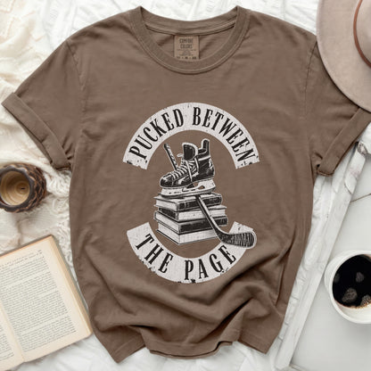 Brown t-shirt with "Pucked Between The Page" text and hockey gear graphic.
