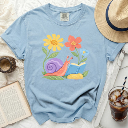 Light blue t-shirt with a cartoon snail reading a book among flowers.