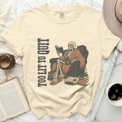 Skeleton reading a book in a chair with the text "TOO LIT TO QUIT".