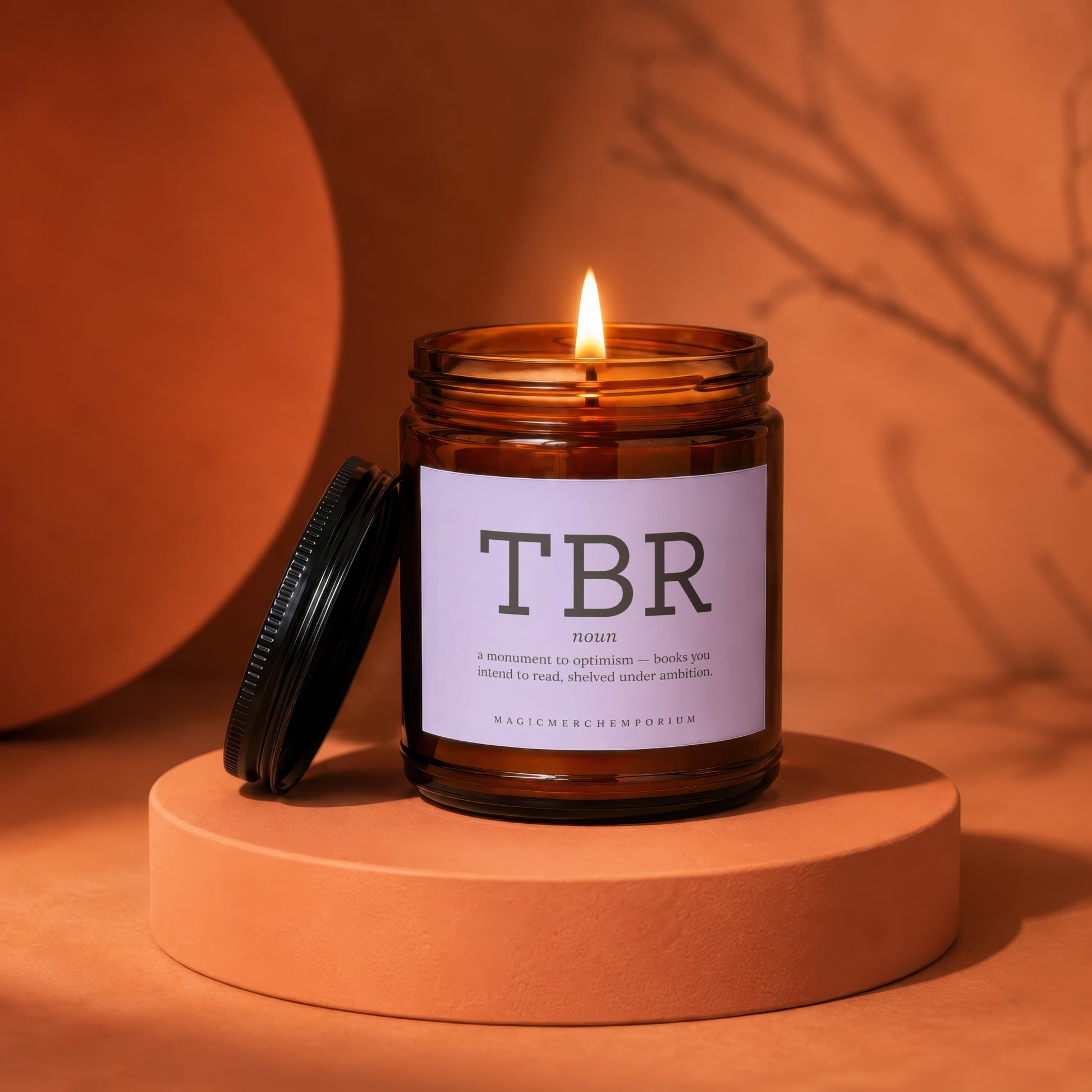 Amber glass candle with lit flame and label: "TBR noun - a monument to optimism"