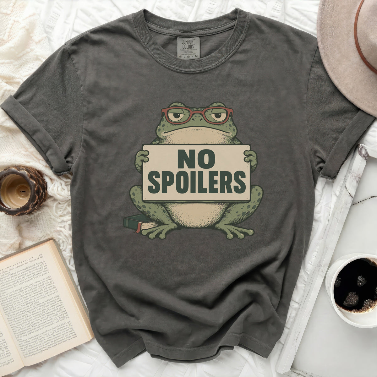 T-shirt with graphic of frog wearing glasses holding a "NO SPOILERS" sign.