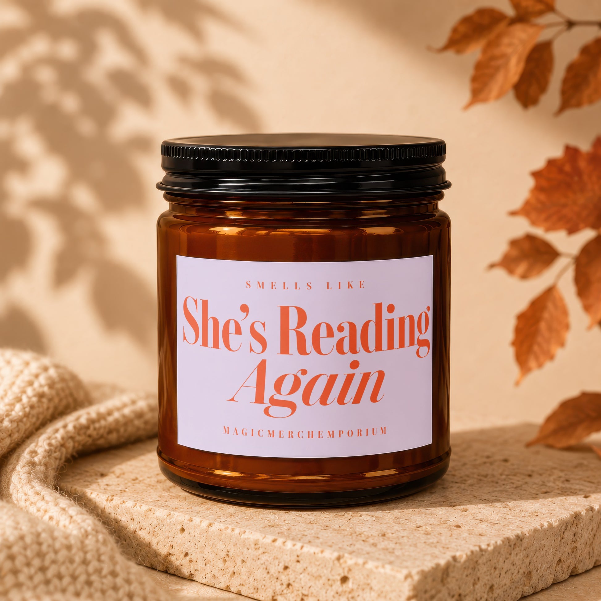 Amber glass candle with "She's Reading Again" text on the label.