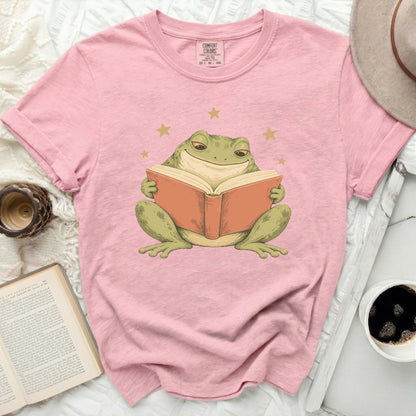 Pink t-shirt with a graphic of a smiling frog reading a book.