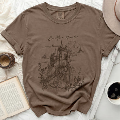 Brown t-shirt with black sketch of a castle and moon, "Be Mine, Monster." text.