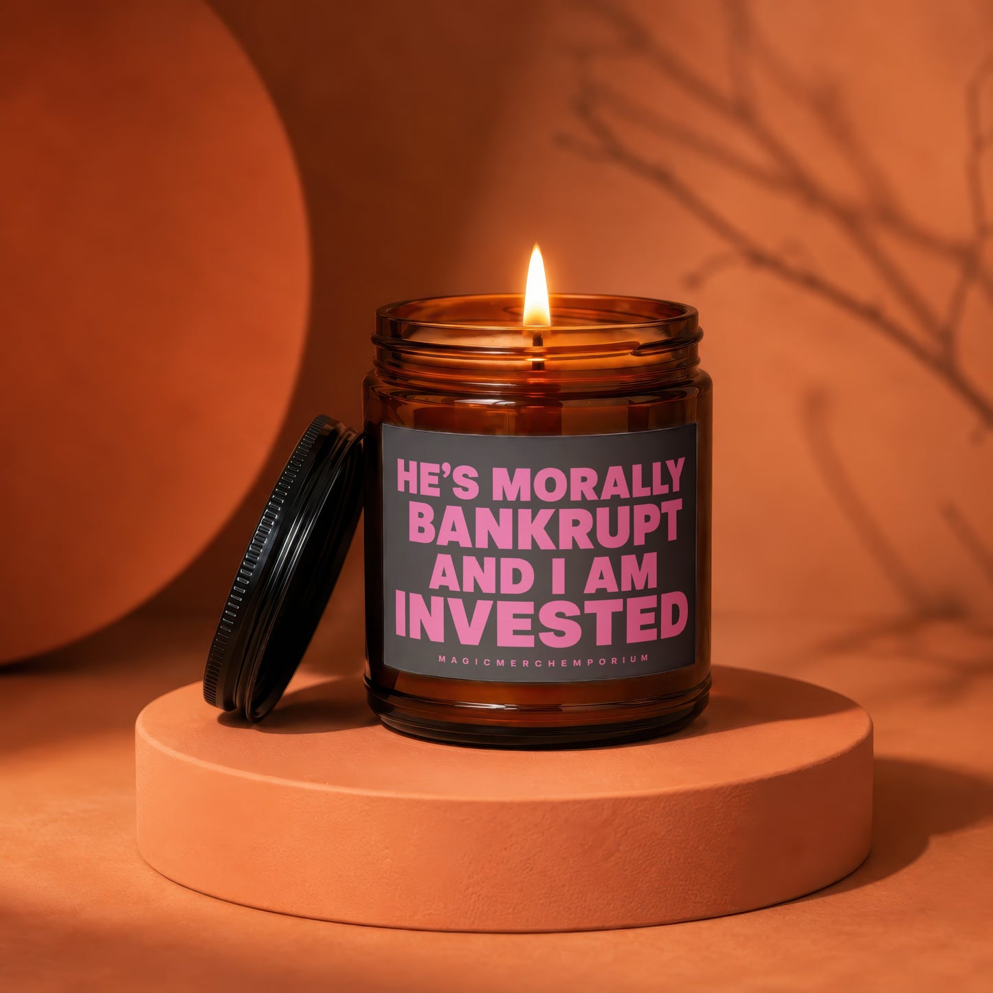 Amber glass candle with lit wick and text: He's morally bankrupt and I am invested.