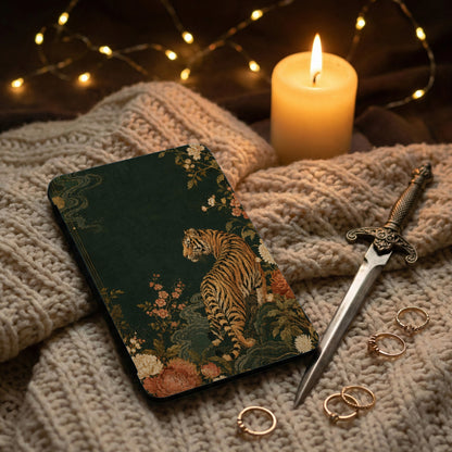 Dark green journal with tiger and floral design, lit candle, rings, and dagger.