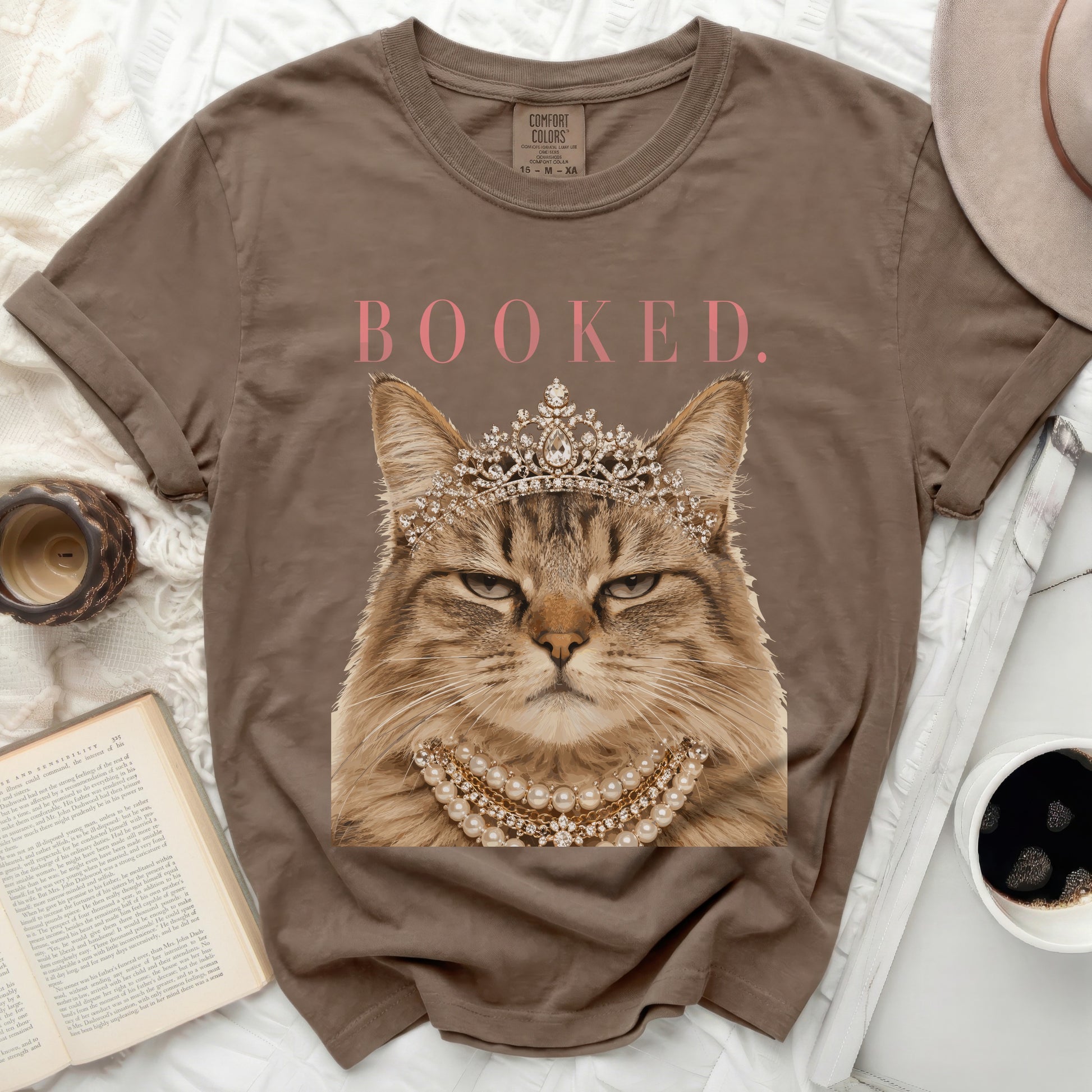 Brown t-shirt with a crowned cat wearing pearls, text "BOOKED."