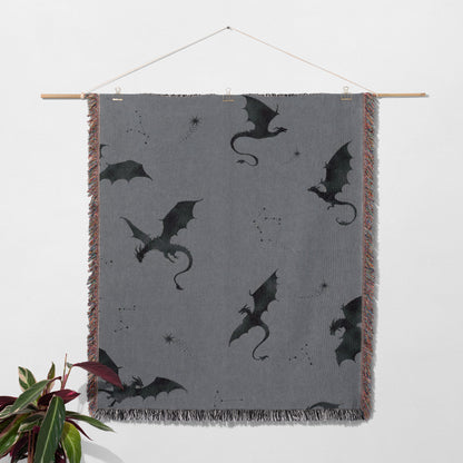 a gray blanket with black dragon silhouettes and some stars printed on it, hanging on a wall.