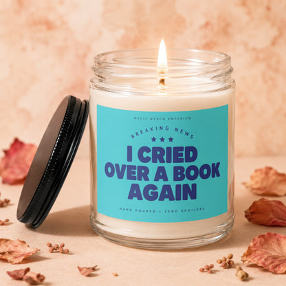 Glass candle with lit wick and blue label reading "I cried over a book again".