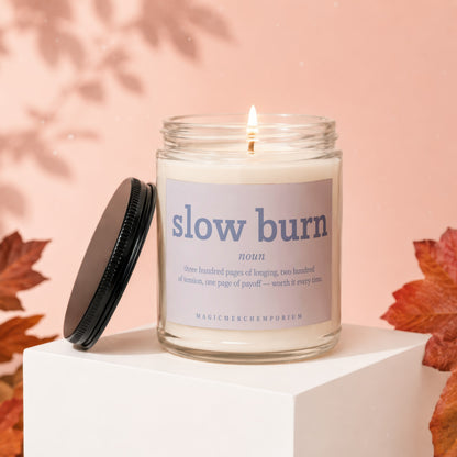 Glass candle with "slow burn" text and definition, on white pedestal with fall leaves.