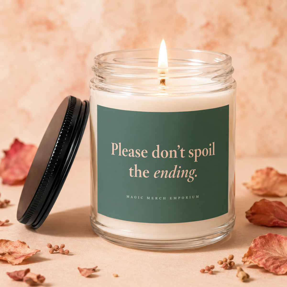 Lit soy candle in a clear glass jar with a dark green label reading Please don’t spoil the ending.