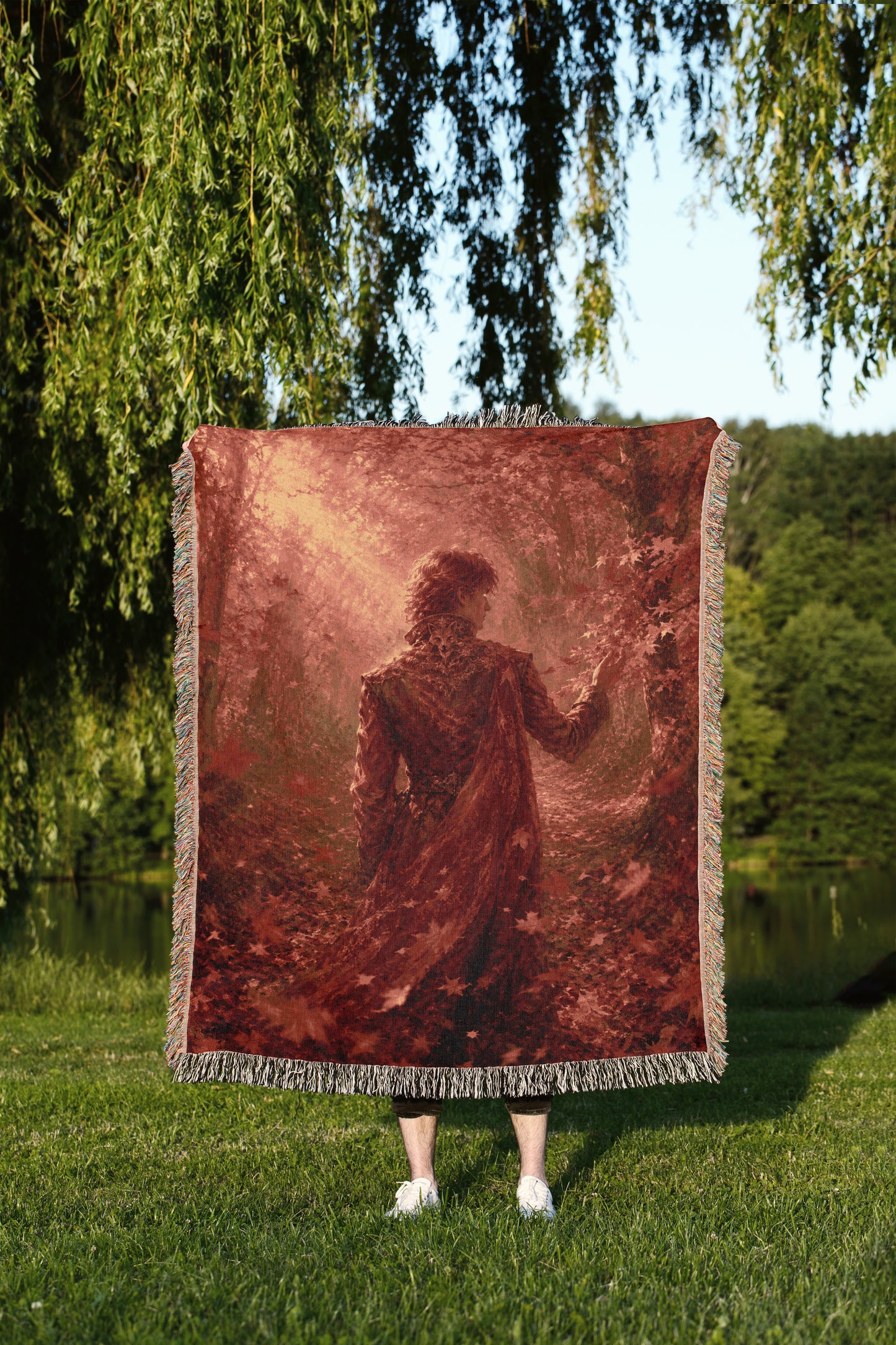 A person stands in a grassy field, holding a large red blanket with a painting of a person on it.
