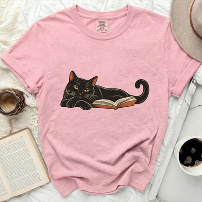 Pink t-shirt with graphic of black cat lying on open book.