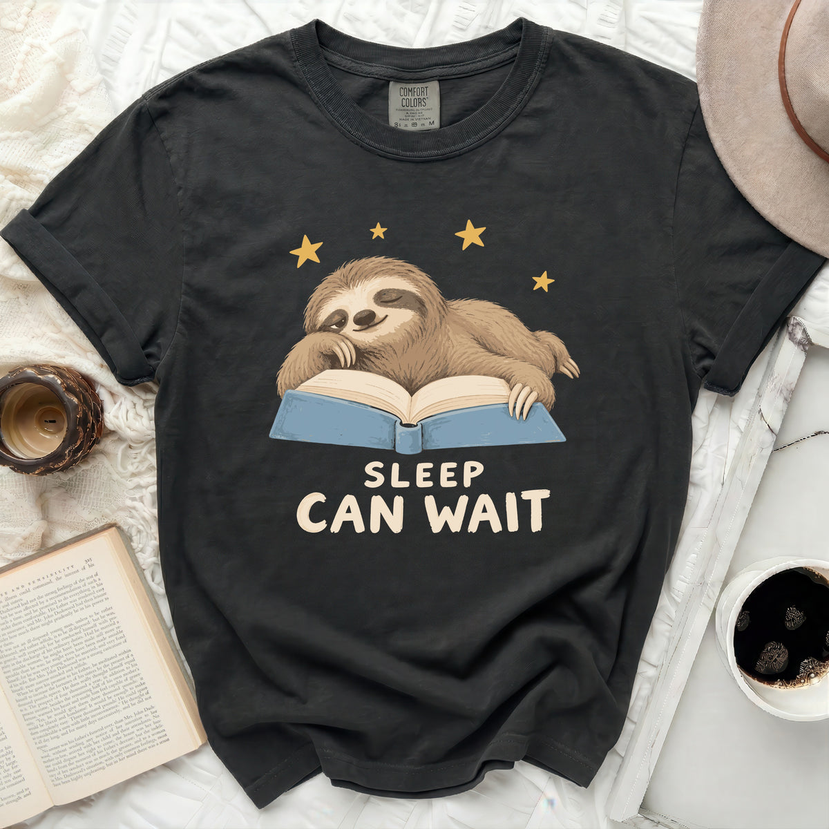 Black t-shirt with a sloth sleeping on an open book and "Sleep Can Wait" text.