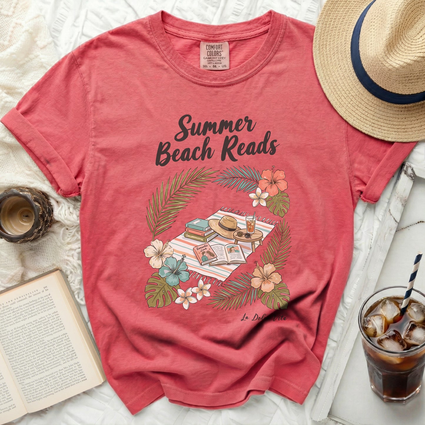 Coral t-shirt with "Summer Beach Reads" graphic featuring books, hat, and tropical foliage.