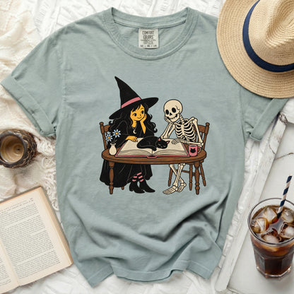 Witch, skeleton, and cat sitting at a table with a book.