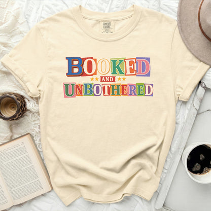 Cream t-shirt with "BOOKED AND UNBOTHERED" in colorful block letters.