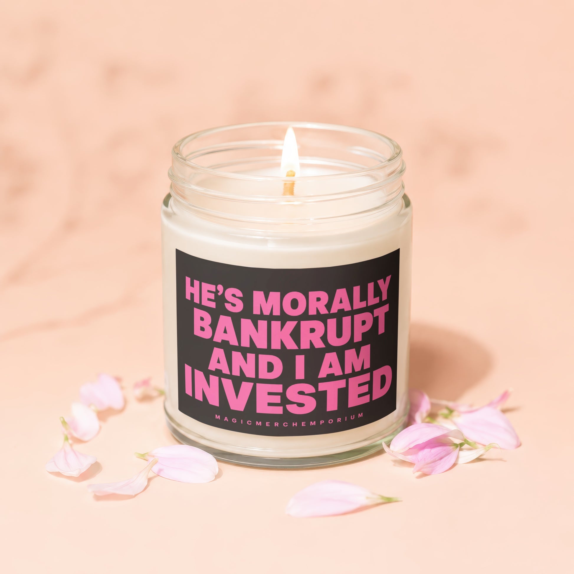 Candle with pink text "He's Morally Bankrupt And I Am Invested" on black label.